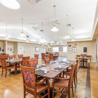 A spacious dining room with elegant tables and chairs, featuring ceiling lights and a wooden floor.