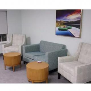 A cozy living room with two armchairs, a sofa, and round tables, complemented by a vibrant artwork on the wall.