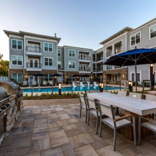 A modern apartment complex featuring a pool and outdoor seating area at sunset.