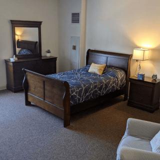 A cozy bedroom featuring a wooden bed, matching dresser with mirror, and a bedside lamp.