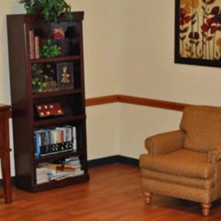 A cozy room corner featuring a bookshelf, a comfortable chair, and a decorative painting.