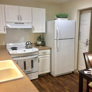 A cozy kitchen with white cabinets, a refrigerator, and a stove, featuring wood flooring.