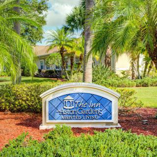 A landscaped area with a decorative sign in front of a building, surrounded by palm trees and gardens.