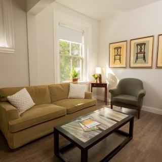 A cozy living room with a sofa, armchair, coffee table, and artwork on the wall.