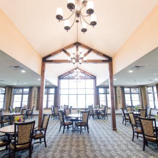 A spacious dining area featuring multiple tables and chairs, illuminated by a chandelier and natural light from large windows.