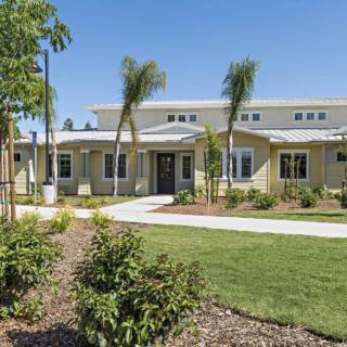 A modern house with a well-maintained lawn and trees under a clear blue sky.