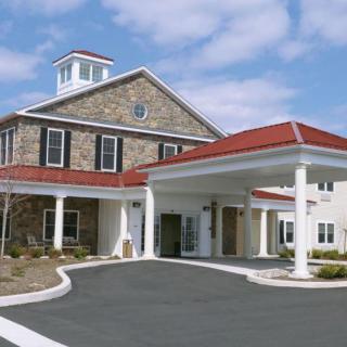 The image shows a building with a stone facade, featuring a grand entrance supported by white columns and a red roof.