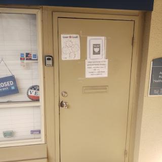 A closed beige door with several signs indicating business hours and access instructions.