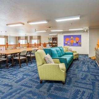 A cozy living room with colorful sofas, a large table, and vibrant artwork on the wall.