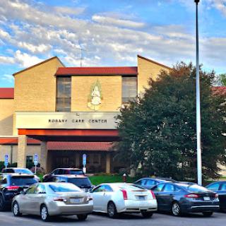A view of a community center with parked cars and a cloudy sky in the background.