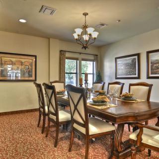 A well-decorated dining room with a large table and elegant chairs, illuminated by a chandelier, featuring framed artwork on the walls.