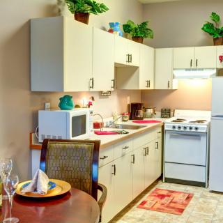A compact apartment kitchen with a microwave, stove, refrigerator, and decorative plants.