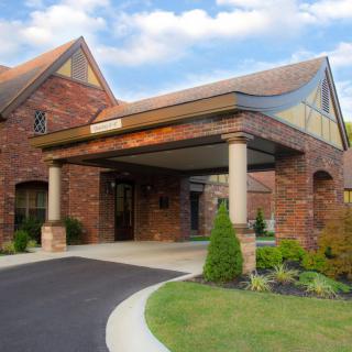 A brick building with a covered entrance and landscaped driveway.