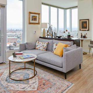 A modern living room with a gray sofa, coffee table, and large windows offering a city view.