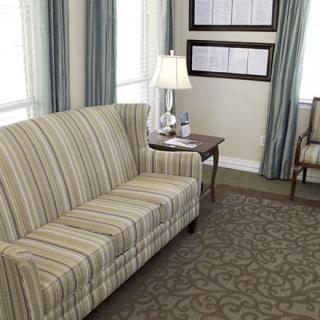 A cozy living room featuring a striped sofa, a table with a lamp, patterned carpet, and elegant curtains.