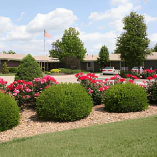 A landscaped garden with blooming flowers and manicured bushes in front of a building on a cloudy day.