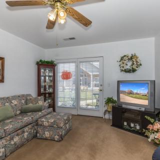A cozy living room with floral-patterned sofa, ceiling fan, and a TV near a glass cabinet.