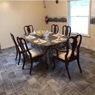 A dining room with a set table and six chairs, featuring tiled flooring and a window.