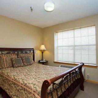 A cozy bedroom with a wooden bed, patterned bedding, a bedside lamp, and a window allowing natural light.