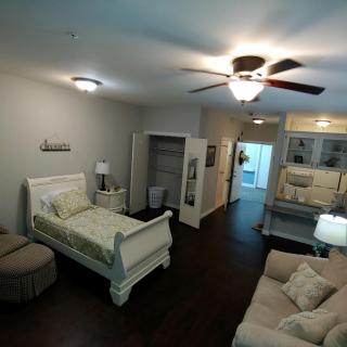 A cozy bedroom featuring a bed, sofa, and ceiling fan with wooden flooring.