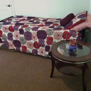 A cozy bedroom with a colorful quilt on the bed and a side table holding a vase.