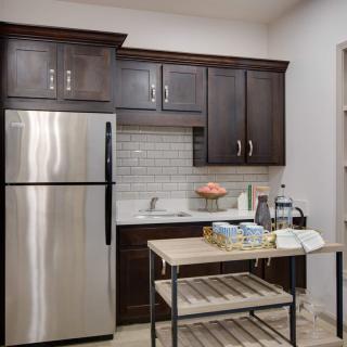 A modern kitchen with dark cabinets, a stainless steel fridge, and a small island cart.