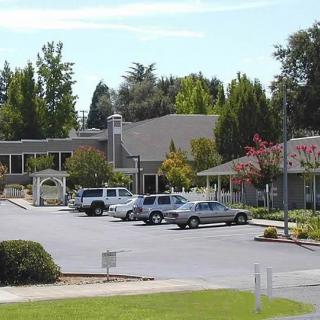 A parking lot with several cars parked in front of buildings surrounded by trees on a sunny day.