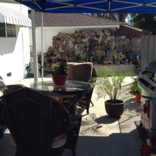 A cozy backyard patio with chairs and potted plants under a shade.