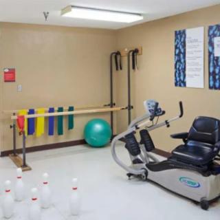 A rehabilitation room featuring various exercise equipment including a stationary bike, colorful therapy bands, an exercise ball, and bowling pins for physical therapy activities.