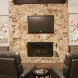 A cozy living room features a stone fireplace with a mounted television above, flanked by two comfortable armchairs.