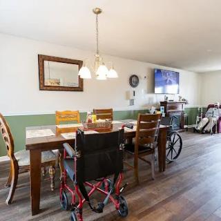 A spacious dining room featuring a large wooden table surrounded by chairs, with a wheelchair positioned at the end, creating an inclusive environment.