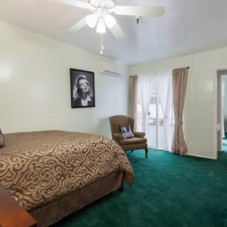 A cozy bedroom featuring a green carpet, decorated with a bed, chair, and wall art.