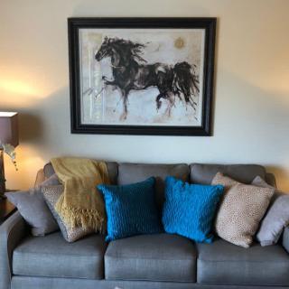 A cozy living room with a gray sofa adorned with colorful pillows, featuring a striking horse painting on the wall.