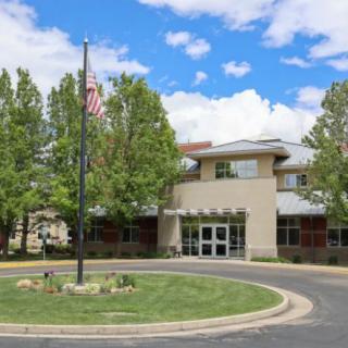 A school building with a flagpole set amidst trees under a partly cloudy sky.