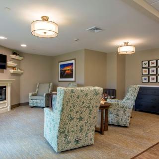 A cozy living room with comfortable chairs, a modern fireplace, artwork on the walls, and soft lighting.