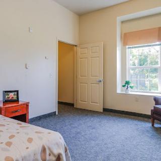 A cozy and simple bedroom featuring a comfortable chair, a nightstand, and natural light from the window.