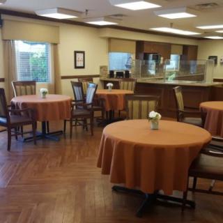 A cozy dining room with round tables covered in orange tablecloths.