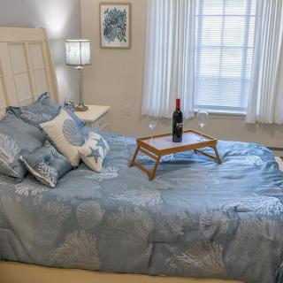 A cozy bedroom setting with a neatly made bed adorned with pillows, featuring a wine bottle on a tray beside a lamp-lit nightstand.