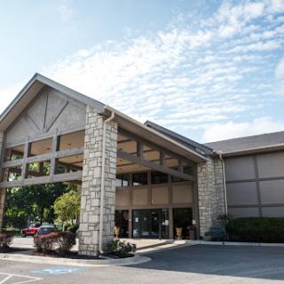 A modern hotel entrance featuring stone accents and lush landscaping under a partly cloudy sky.