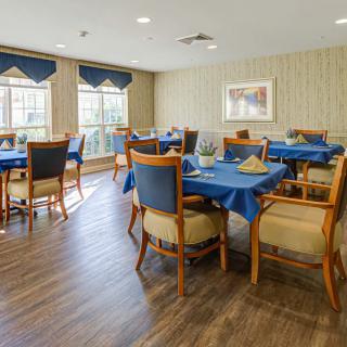 A dining room with tables and chairs set up, featuring blue tablecloths and wooden furniture.