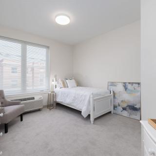 A minimalist bedroom with a single bed and soft neutral tones, featuring an armchair and wall art.