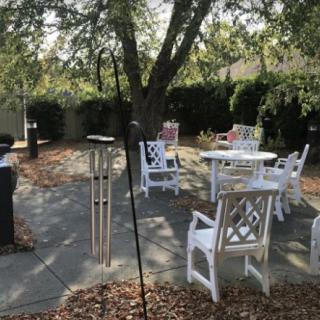 A peaceful backyard patio area featuring white chairs and tables under a tree.