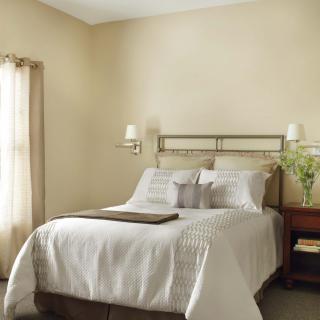 A cozy bedroom with neutral tones, featuring a neatly made bed and a nightstand adorned with flowers.