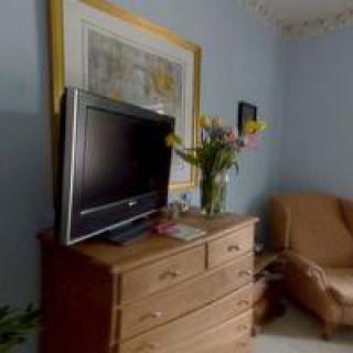 A cozy living room corner featuring a dresser with a television, flowers, and artwork.