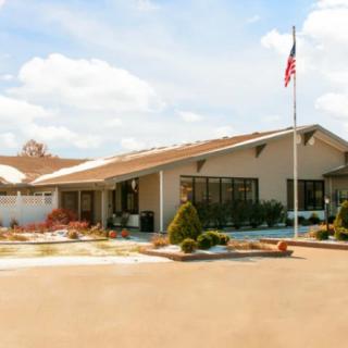 A single-story building with an American flag flying in front, surrounded by landscaped grounds and a parking area.