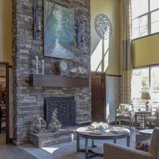 A cozy living room with a stone fireplace, large artwork, and ample natural light from expansive windows.