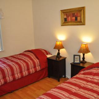 A cozy bedroom with twin beds adorned with red bedding and warm lighting from two lamps on the nightstands.