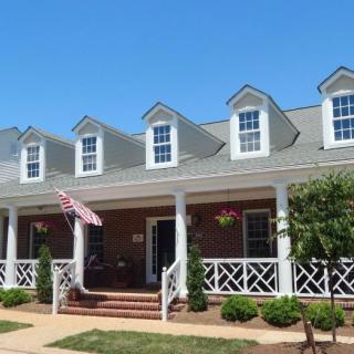 A colonial-style house with brick exterior and white trim, featuring a front porch adorned with columns and roof dormers.