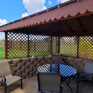 A cozy outdoor gazebo with a table and chairs, surrounded by a lush landscape.