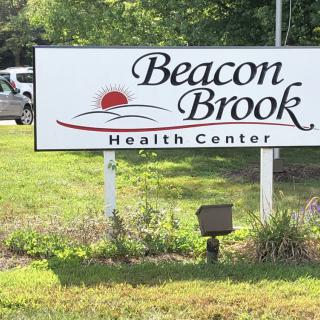 A sign for Beacon Brook Health Center surrounded by grass and plants.